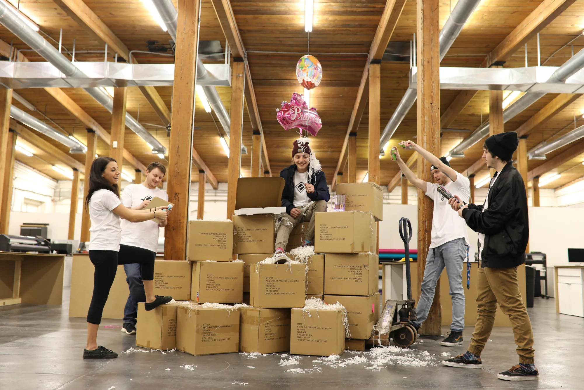His birthday in the warehouse — a throne of boxes, a Princess balloon, and the whole crew with the silly string